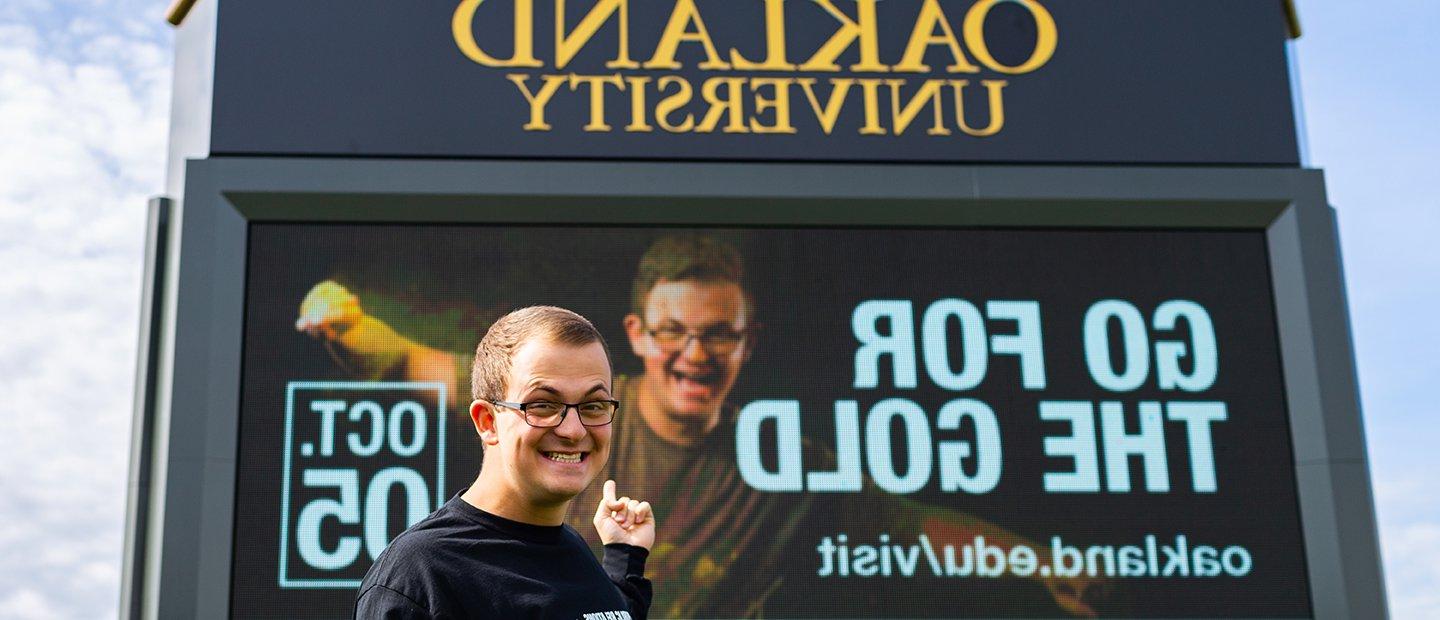 Young man pointing to an ad that he is featured in on an 韦德体育app官网 electronic marquee.