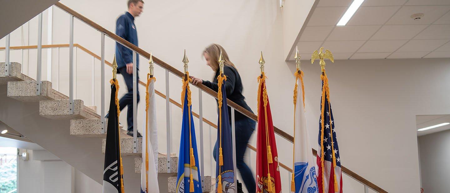 Armed forces flags appear in front of a staircase in a campus building.